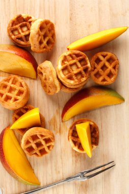 Daire ahşap kesme tahtası üzerinde mango ile mini waffle. Üstten görünüm