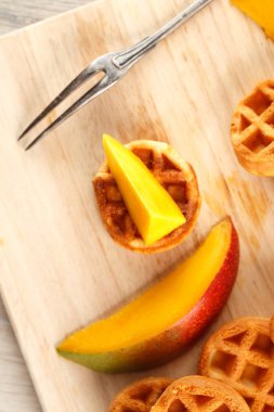 Daire ahşap kesme tahtası üzerinde mango ile mini waffle. Üstten görünüm