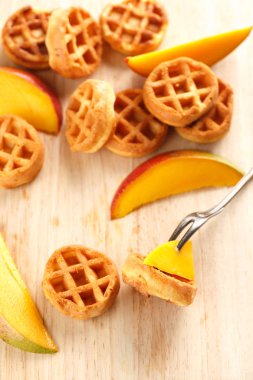 Daire ahşap kesme tahtası üzerinde mango ile mini waffle. Üstten görünüm