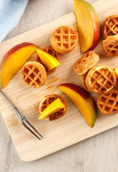 Daire ahşap kesme tahtası üzerinde mango ile mini waffle. Üstten görünüm