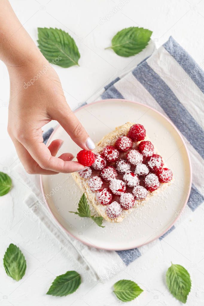 girl puts fresh raspberries on Napoleon cake