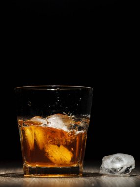 Ahşap bir masa üzerinde bardakta viski sıçrama. Siyah arka plan üzerine. Portre