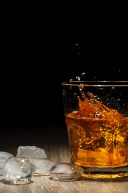Ahşap bir masa üzerinde bardakta viski sıçrama. Siyah arka plan üzerine. Portre