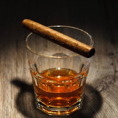 Bir bardak buz küpleri ve ahşap bir masa üzerinde bir puro ile alkollü içecek. Siyah arka plan üzerine bardakta viski