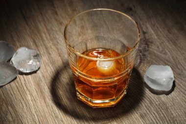 Ahşap masa buz küpleri ile alkollü içecek bir bardak. Siyah arka plan üzerine bardakta viski