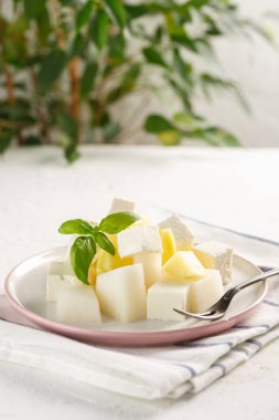 Peynirli meyve salatası. Mango, kavun peynir ve fesleğen ile beyaz arka plan üzerinde bir plaka üzerinde