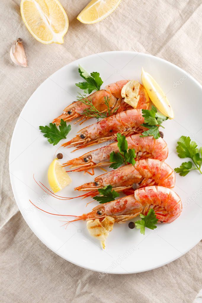 Grilled shrimps with spice, lemon and greenery on white plate. Grilled seafood.