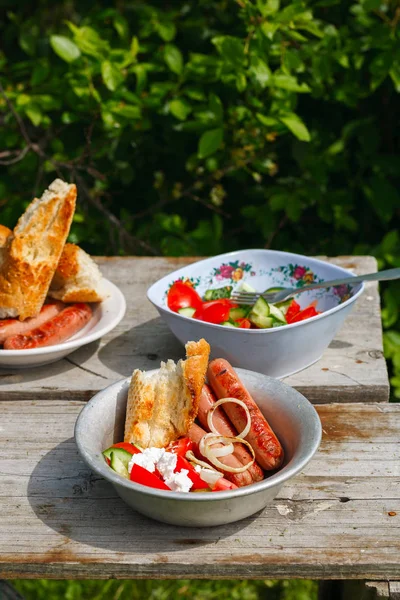 Churrasco. Almoço. salsichas grelhadas com salada de legumes, cebola e pão grelhado . — Fotografia de Stock