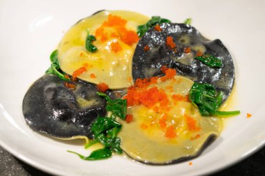 Sarı ve siyah ravioli, havyar ve beyaz tabakta ıspanak.