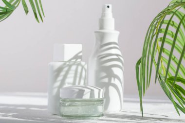 Güneşli bir günde palmiye yapraklarının gölgesinde beyaz kozmetik tüpleri. Kozmetik ürünleri için konteynır. Cilt bakımı ve güzellik kavramı.