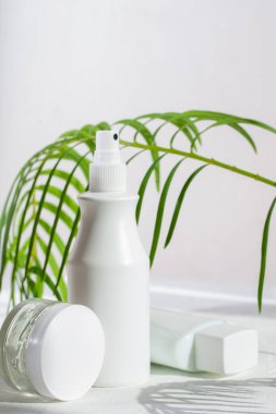 Güneşli bir günde palmiye yapraklarının gölgesinde beyaz kozmetik tüpleri. Kozmetik ürünleri için konteynır. Cilt bakımı ve güzellik kavramı.