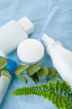 Mavi arka planda yeşil yapraklarla süslenmiş beyaz kozmetik kaplar. Model-up. Güzellik tedavisi
