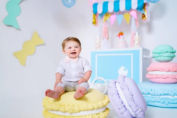 Retrato de menino muito adorável sentado no grande macaroon e sorrindo . — Fotografia de Stock