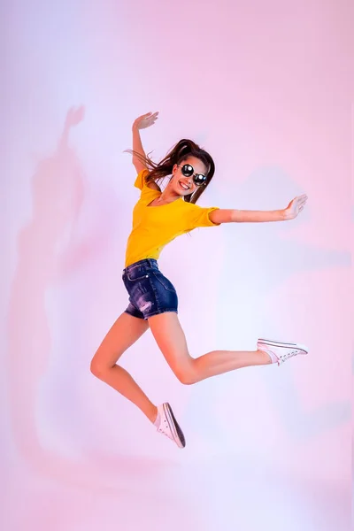 Success, dream, femenine girlish life concept. Excited brunette lady model is jumping up, wearing casual clothes, white shoes