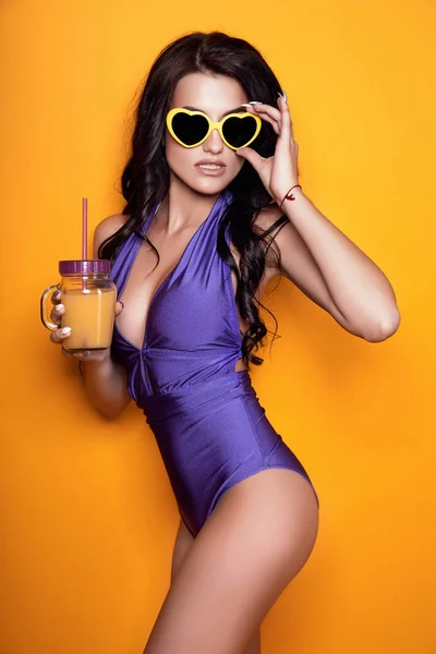 Immagine di giovane donna sorridente in costume da bagno isolato su sfondo giallo con cocktail in mano . — Foto Stock