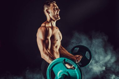 Atletik erkek egzersizleri, pazı dumbbells ile yapıyor. Koyu arka plan üzerinde çıplak gövde ile güçlü erkek fotoğrafı. Güç ve motivasyon.
