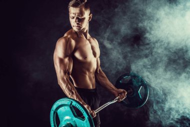 Atletik erkek egzersizleri, pazı dumbbells ile yapıyor. Koyu arka plan üzerinde çıplak gövde ile güçlü erkek fotoğrafı. Güç ve motivasyon.