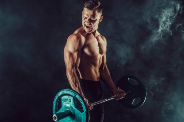Atletik erkek egzersizleri, pazı dumbbells ile yapıyor. Koyu arka plan üzerinde çıplak gövde ile güçlü erkek fotoğrafı. Güç ve motivasyon.