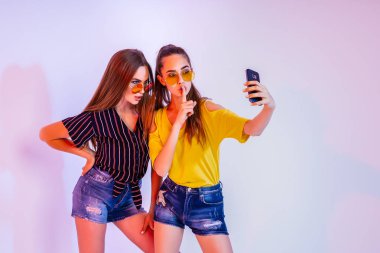 İki genç kadın olduğunu stüdyoda ayakta ve beyaz arka plan üzerinde selfie smartphone ile yapma güneş gözlüğü