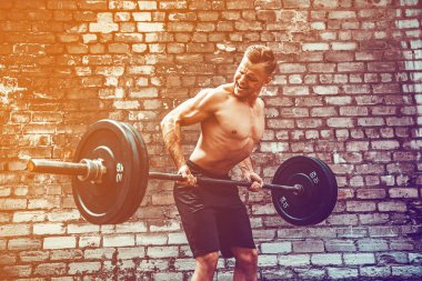 Atletik bir adam bir halter ile çalışma dışarı. Güç ve motivasyon. Arka kasları için egzersiz