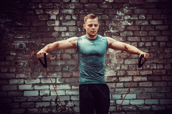 Fitness man exercising with stretching band in outdoor gym.