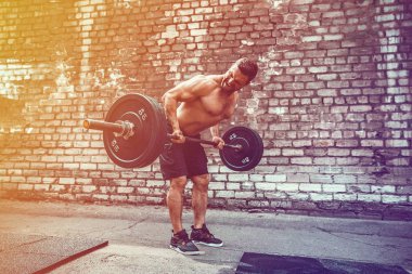 Atletik bir adam bir halter ile çalışma dışarı. Güç ve motivasyon. Arka kasları için egzersiz