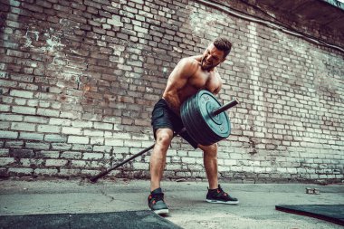 Atletik bir adam bir halter ile çalışma dışarı. Güç ve motivasyon. Arka kasları için egzersiz