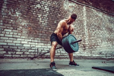 Atletik bir adam bir halter ile çalışma dışarı. Güç ve motivasyon. Arka kasları için egzersiz