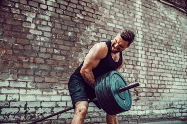 Atletik bir adam bir halter ile çalışma dışarı. Güç ve motivasyon. Arka kasları için egzersiz