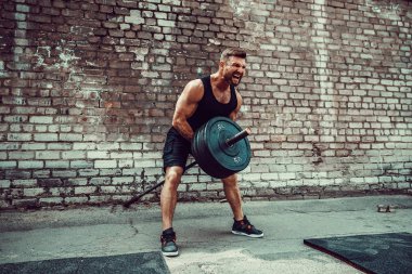 Atletik bir adam bir halter ile çalışma dışarı. Güç ve motivasyon. Arka kasları için egzersiz