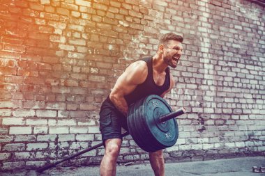 Atletik bir adam bir halter ile çalışma dışarı. Güç ve motivasyon. Arka kasları için egzersiz