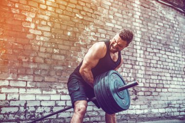 Atletik bir adam bir halter ile çalışma dışarı. Güç ve motivasyon. Arka kasları için egzersiz