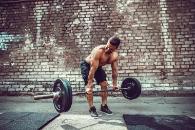 Atletik bir adam bir halter ile çalışma dışarı. Güç ve motivasyon. Arka kasları için egzersiz