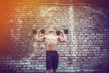 kaslı adam bir tuğla duvara dumbbell ile yapıyor