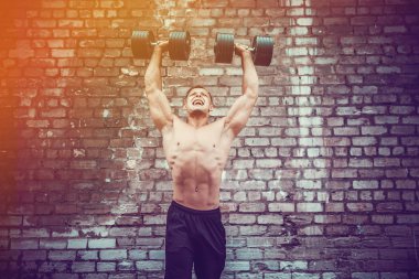 kaslı adam bir tuğla duvara dumbbell ile yapıyor