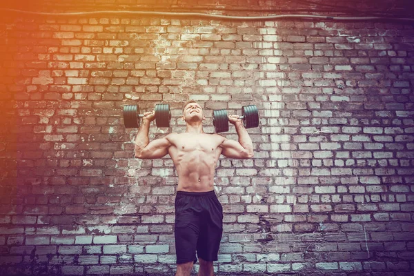 Svalnatý chlap dělá cvičení s činka proti cihlové zdi — Stock fotografie
