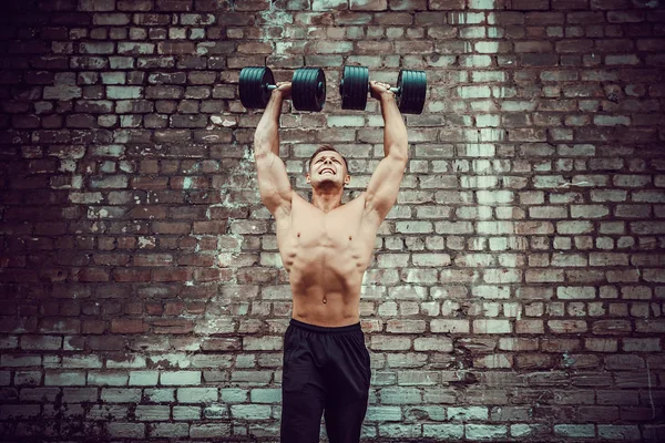 Gespierde man doen oefeningen met dumbbell tegen een bakstenen muur — Stockfoto