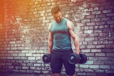 kaslı adam bir tuğla duvara dumbbell ile yapıyor