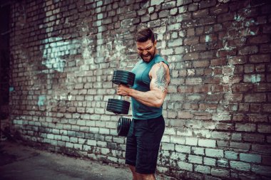 kaslı adam bir tuğla duvara dumbbell ile yapıyor