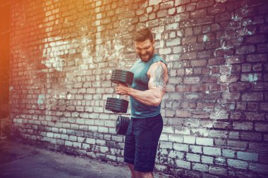kaslı adam bir tuğla duvara dumbbell ile yapıyor