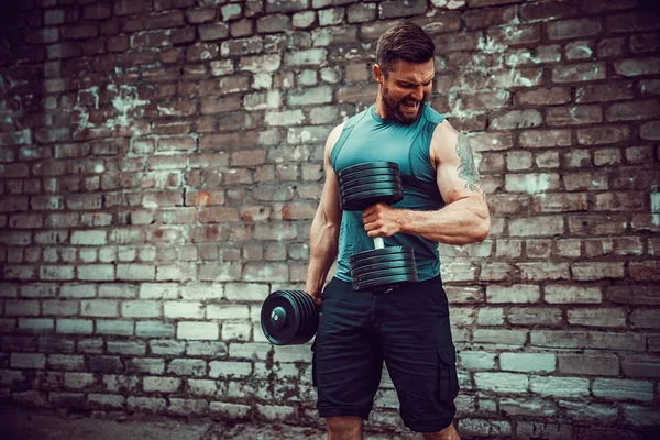 Musculoso chico haciendo ejercicios con mancuerna contra una pared de ladrillo — Foto de Stock