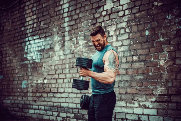 Muskulöser Typ, der Übungen mit der Hantel gegen eine Ziegelwand macht — Stockfoto
