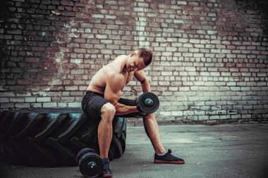 kaslı adam bir tuğla duvara dumbbell ile yapıyor