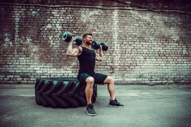 kaslı adam bir tuğla duvara dumbbell ile yapıyor