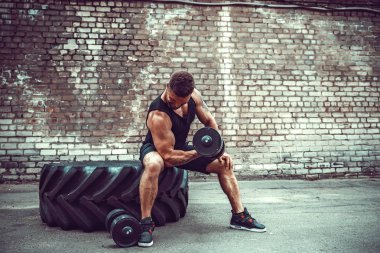 kaslı adam bir tuğla duvara dumbbell ile yapıyor