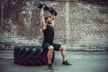 kaslı adam bir tuğla duvara dumbbell ile yapıyor