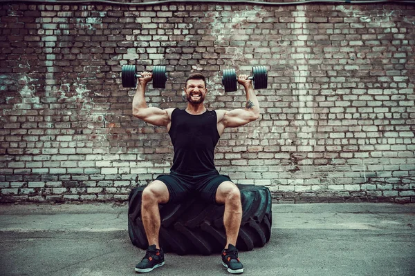 Musclé gars faire des exercices avec haltère contre un mur de briques — Photo