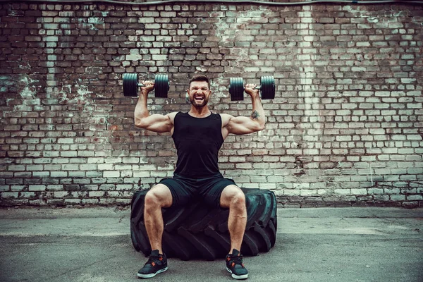 Gespierde man doen oefeningen met dumbbell tegen een bakstenen muur — Stockfoto