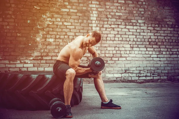 Musculoso chico haciendo ejercicios con mancuerna contra una pared de ladrillo — Foto de Stock