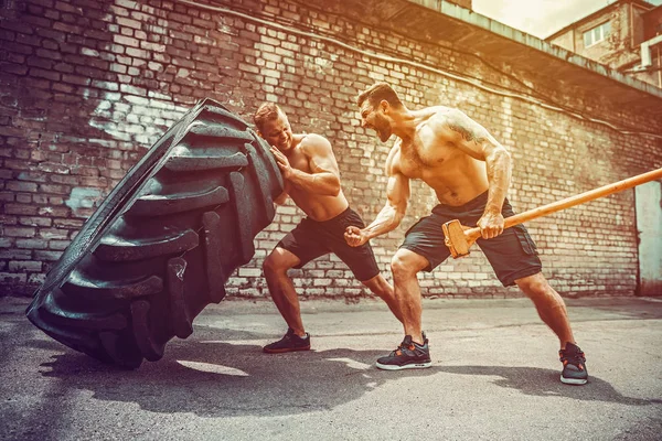 Two muscular athletes training. Muscular fitness shirtless man moving large tire — Stock Photo, Image